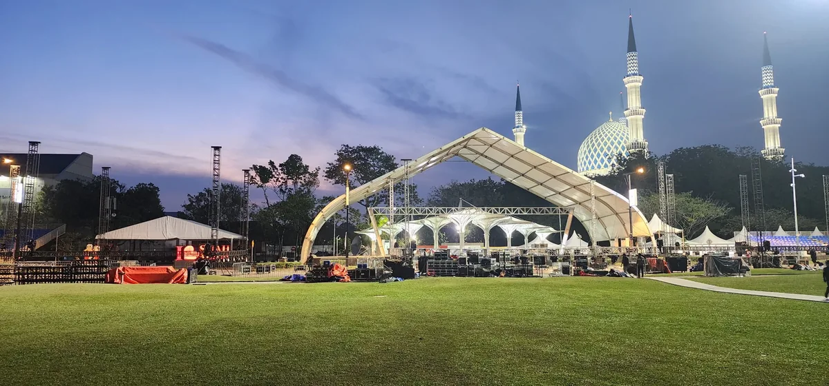 Arched stage canopy on a lawn beside a mosque at dusk