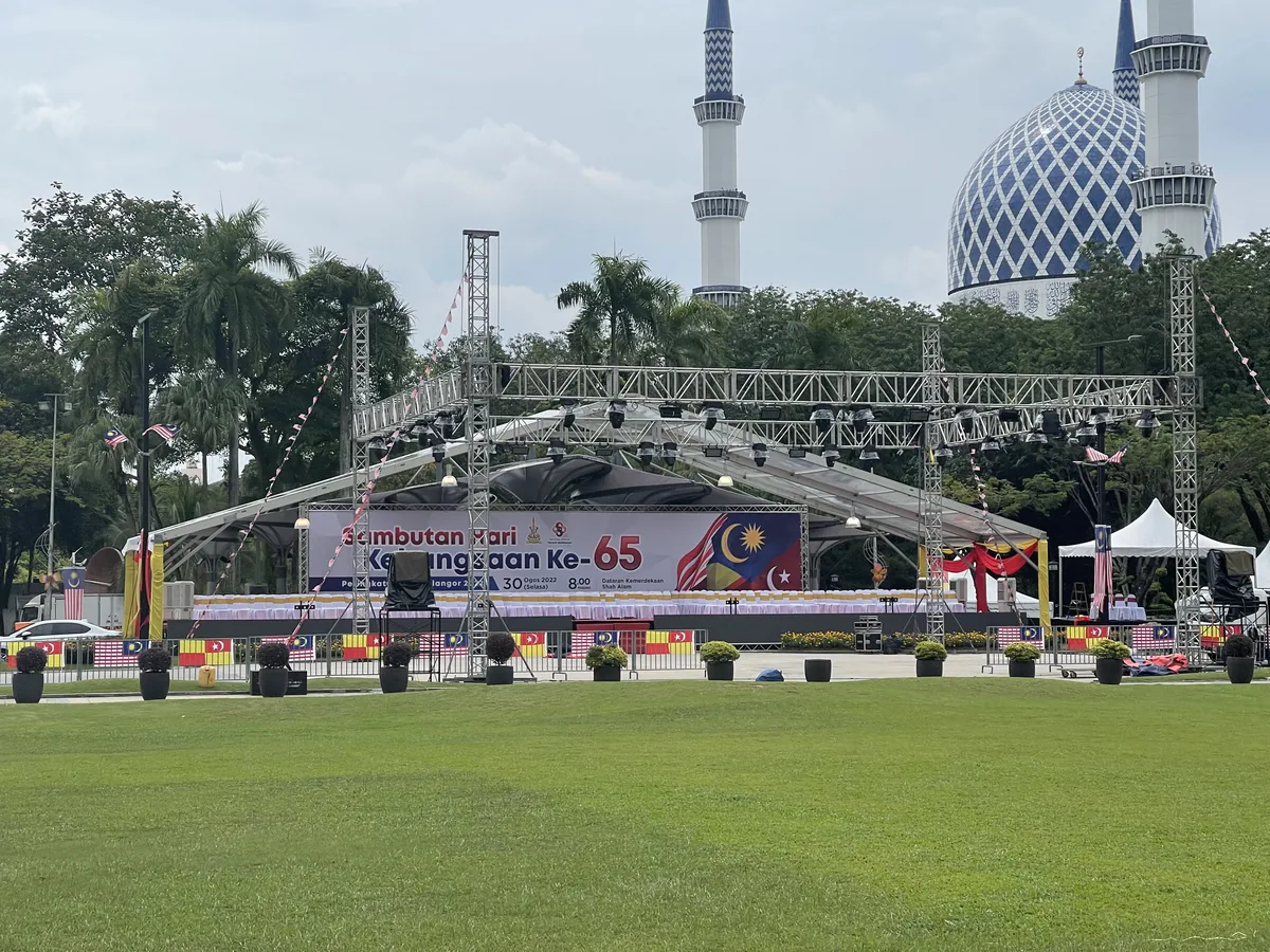 Truss stage with a national day banner in front of a blue-domed mosque