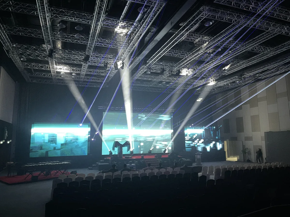 White moving-head beams over a stage with three LED screens