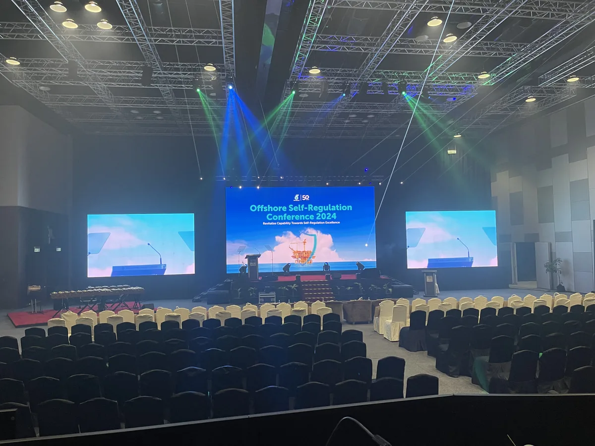Three LED screens with light beams above an empty hall