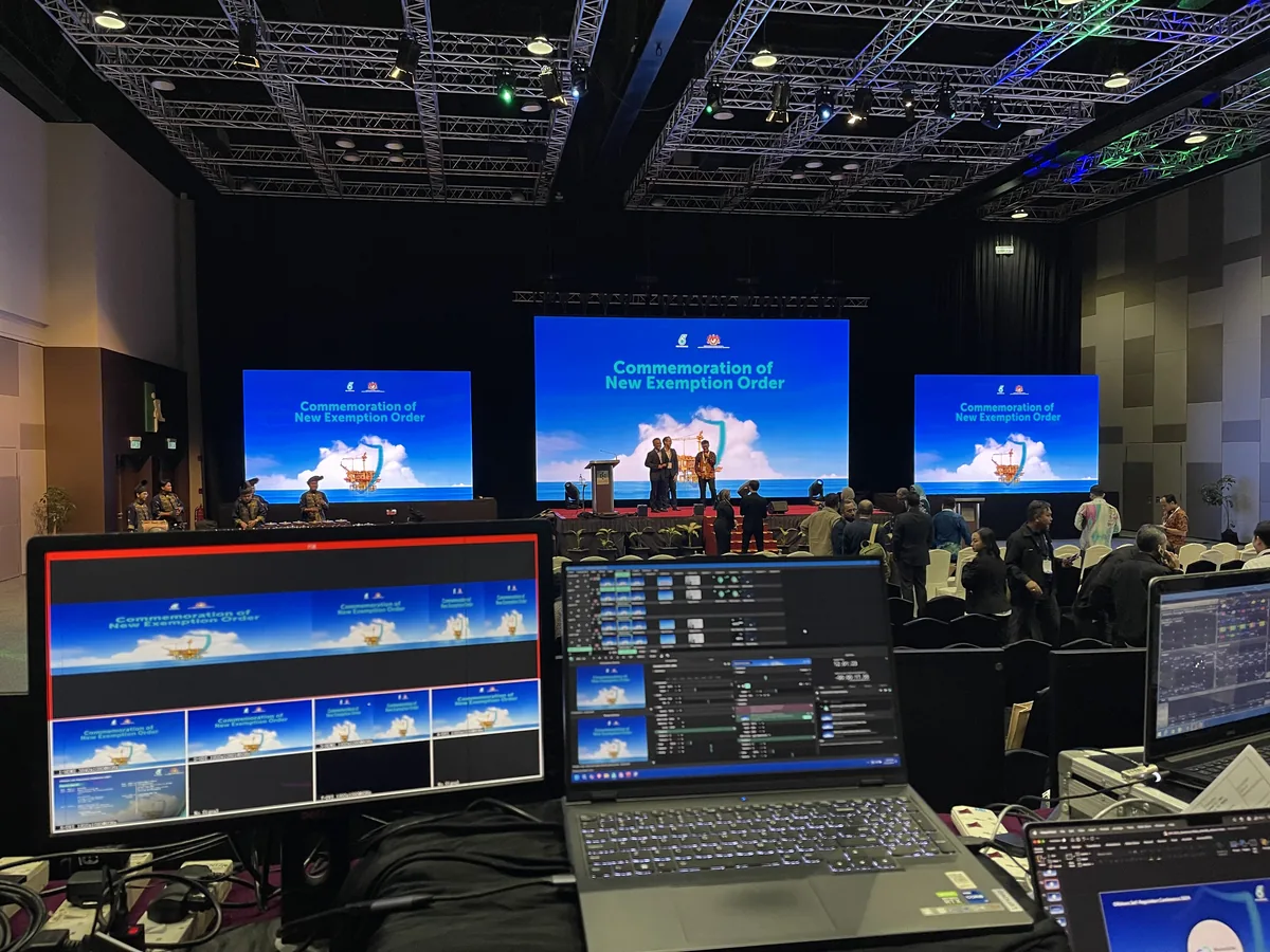 Laptops and monitors at a control desk with stage screens beyond