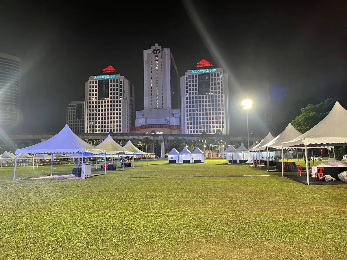 Lit white tents on a field in front of city towers at night