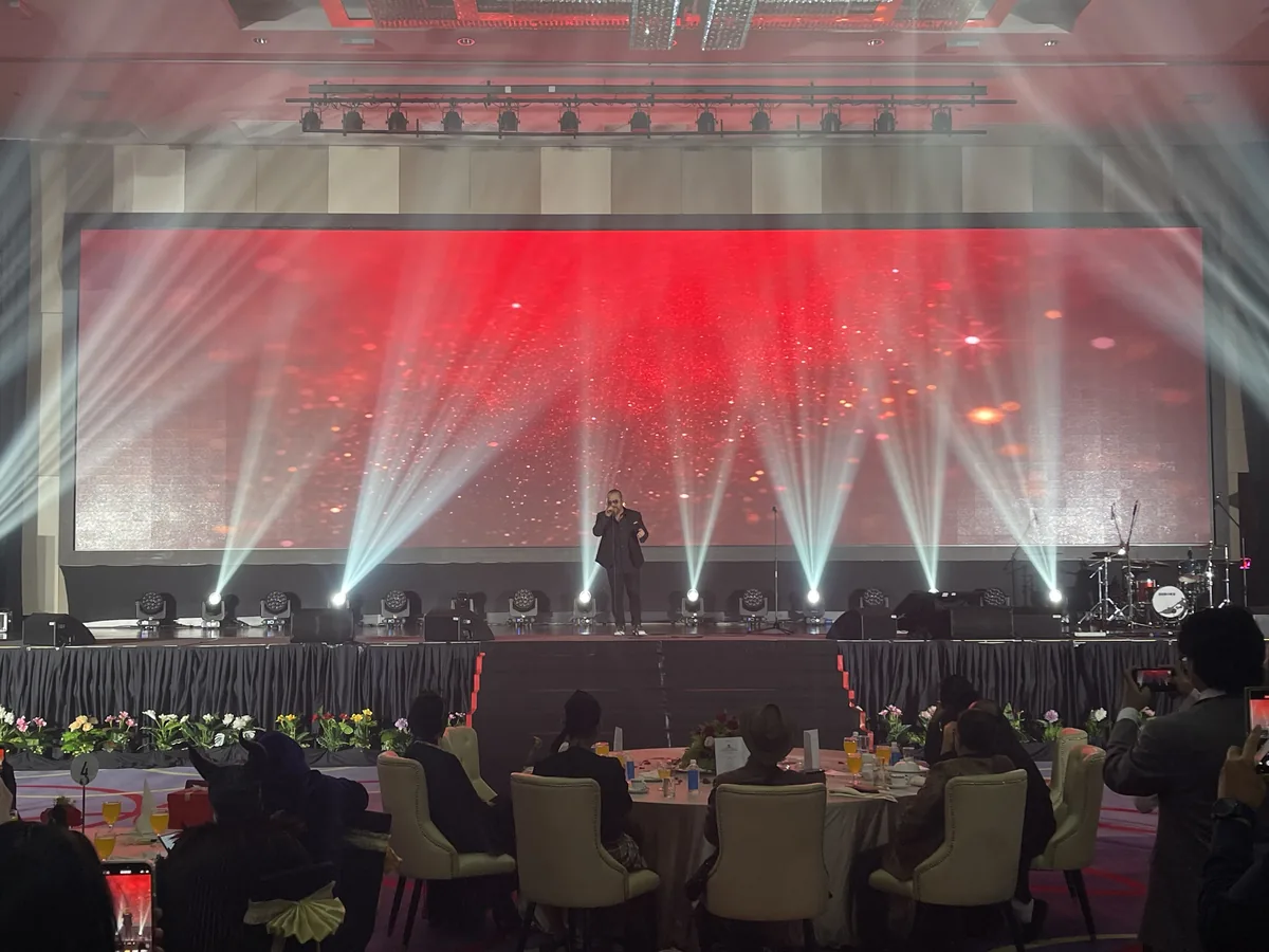 Performer on stage with white beams over seated dinner guests
