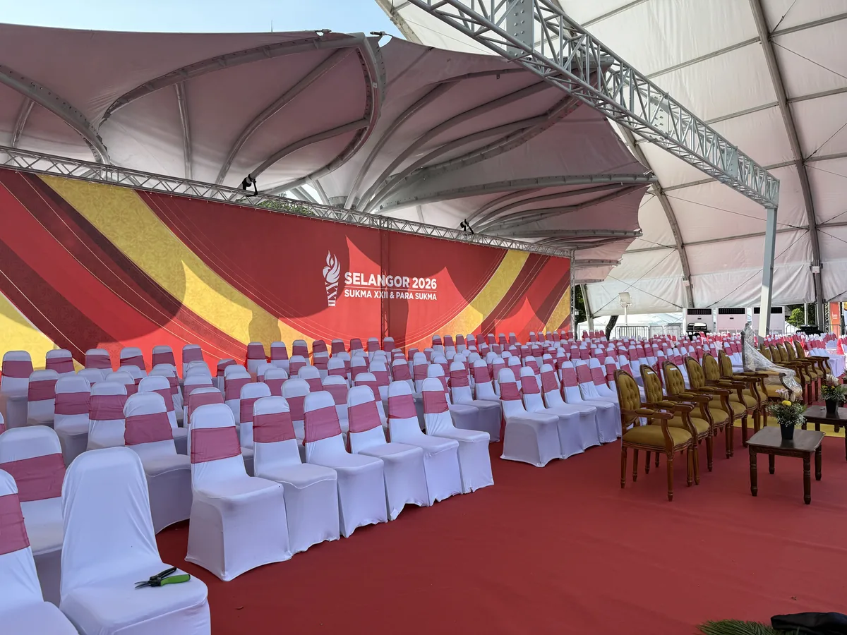 Marquee seating with pink-sashed chairs on red carpet facing a backdrop